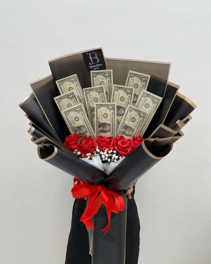 A large decorative hand-held bouquet crafted completely from crisp green banknotes rolled into rosettes and arranged alongside faux white roses and gold ribbon accents.